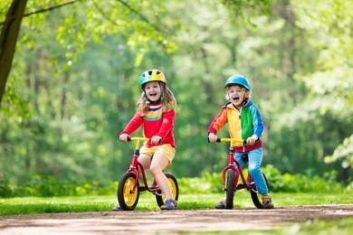 children riding balance bike. kids on bicycle in sunny park. little girl and boy ride glider bike on warm summer day. preschooler learning to balance on run bicycle in safe helmet. sport for kids