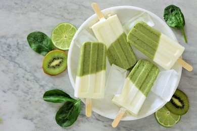 healthy green smoothie popsicles with kiwi, lime and spinach on a white marble plate, overhead view