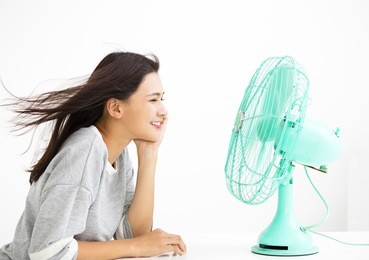 smiling woman cooling herself by electric fan