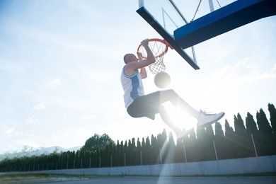young man jumping and making a fantastic slam dunk playing stree