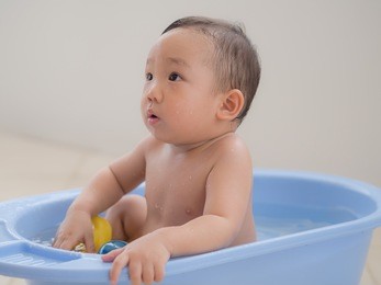 happy 1-year old asian baby boy splashing in the water and  playing with toy in little plastic bath outdoors
