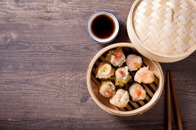 hot chinese dim sum in a bamboo steamer with sauce and chopsticks on wooden table, chinese food