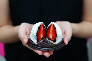 hand holding a tray of strawbery diafuku (ichigo daifuku or mochi) is japanese confectionery, rice cake stuffed with sweetened red bean and fresh strawberry, japanese traditional dessert.