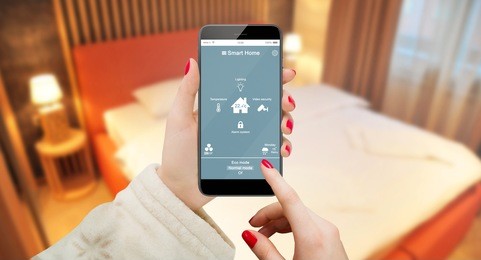 smart home app on phone hold by female hand with bedroom interior in background