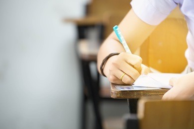 closeup hands university student holding pen writing doing examination with blurred background.students in uniform attending exam classroom educational school.space for text.