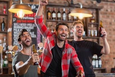 happy male friends cheering while holding beer bottles in bar