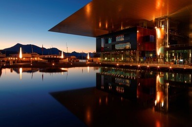morning scenery of lucerne at sunrise with reflections of the beautiful culture & congress center on the water, silhouettes of distant mountains & the golden light of dawning sky glowing above horizon
