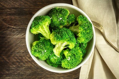 a bowl of cooked green broccoli with sea salt, shot from above on a dark wooden rustic texture with a place for text