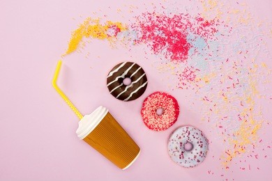 top view of coffee cup and variety frosted donuts isolated on pink. donuts and coffee background