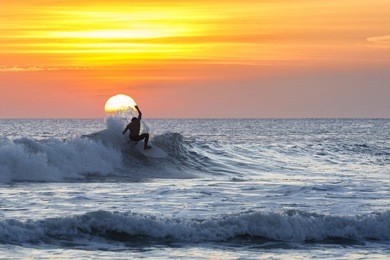 a surfer rides a wave during sunset at kuta beach, bali