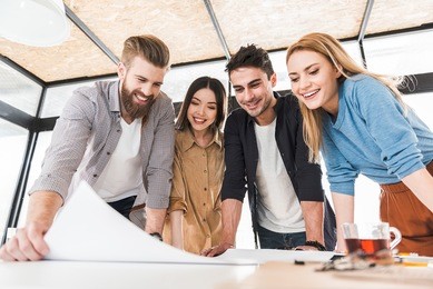 result of job. jolly smiling co-workers are inclining on table. they looking at sheet of paper. low angle
