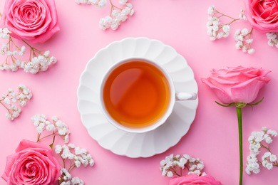 cup of tea with fresh flowers on pink background. top view. copy space.