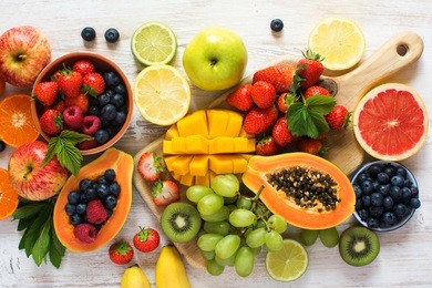 different rainbow colored fruits, strawberries, blueberries, mango, orange, grapefruit, banana, apple, grapes, kiwis on the white background, above view, selective focus
