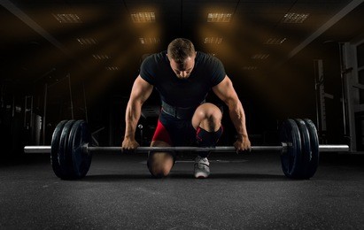 athlete is standing on his knee and near the bar in the gym and is preparing to make a deadlift