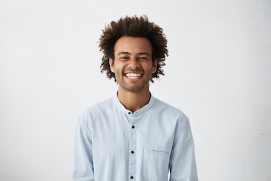 handsome unshaven young dark-skinned male laughing out loud at funny meme he found on internet, smiling broadly, showing his white straight teeth. positive human facial expressions and emotions