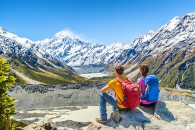 backpackers couple hiking looking at mt cook view on mountains tramping in new zealand. people hikers relaxing during hike in alps of south island.