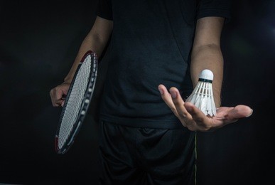 man is holding the shuttlecock and the badminton racket. in dark background