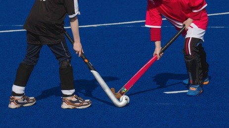 two children players of field hockey contesting the ball on blue wet turf field