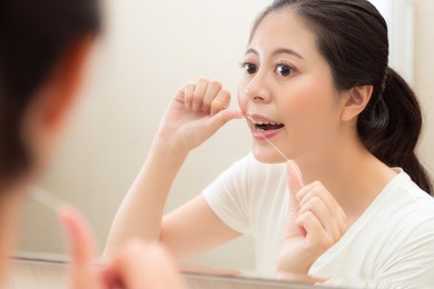 closeup photo of attractive elegant girl using floss clean tooth gap avoid remaining food on teeth with mirror reflection image in bathroom.