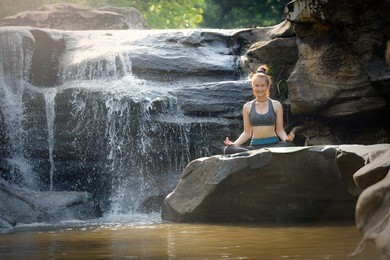 asian teenage girls are exercising, doing body shaping fitness, and meditating with yoga on rocks near waterfalls in high mountain rainforests. health and nature concept.