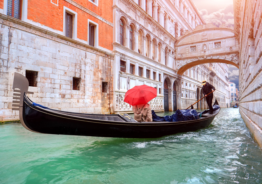 woman with a red umbrella in gondola passing over bridge of sighs in venice, italy