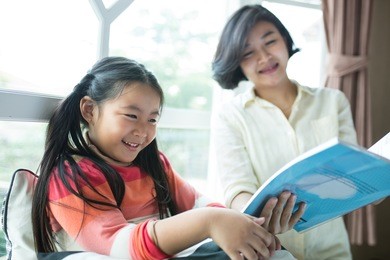 asian children reading book with her mother in living room.
