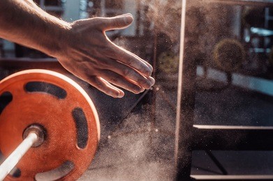male powerlifter hand in talc and sports wristbands preparing to bench press. hands in chalk. with a barbell. in clap. activity, arm, athlete, backlit, barbell, chalk, clapping, closeup, workout