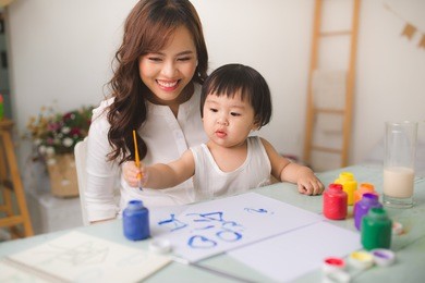 happy family mother and daughter together paint. asian woman helps her child girl.