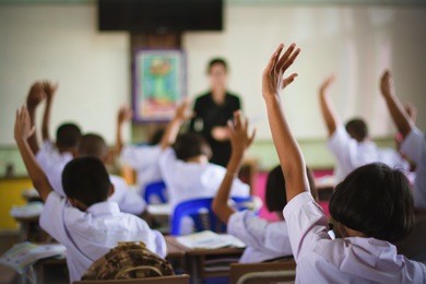 education, elementary school, learning and people concept - group of school kids with teacher standing in classroom and raising hands