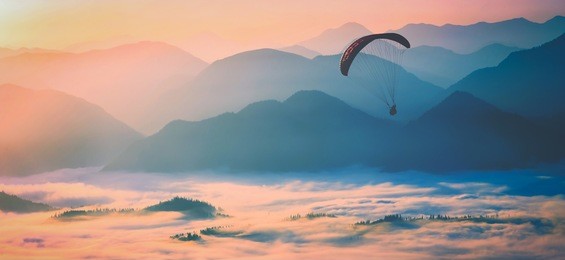 paraglide silhouette flying over the misty mountain valley in a light of sunrise. instagram stylization.