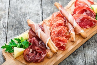 antipasto platter cold meat plate with grissini bread sticks, prosciutto, slices ham, beef jerky, salami and arugula on cutting board on wooden background. meat appetizer