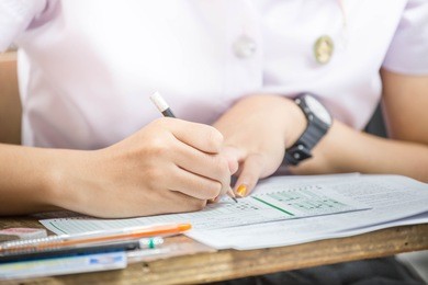 soft focus undergraduate student holding pencil and sitting on row chair doing final exam attending in examination room or classroom.university student in uniform.