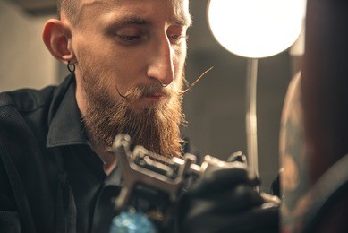 portrait of male master demonstrating thoughtfulness. he doing tattoo on arm of client