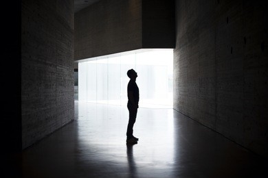 lonely silhouette in dark architecture with light background. horizontal image. full body of man in profile. mystery photo.