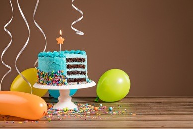 chocolate birthday cake with blue buttercream icing and colorful balloons on a brown background.