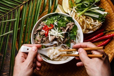 pho bo soup with beef and chopsticks in male hands close-up