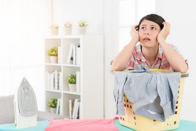 lovely beautiful lady using iron sort out family clothes feeling bored and leaning on clothing basket thinking travel planning for relaxing at home.