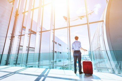 businessman at airport terminal boarding gate looking at airplane flying through the window