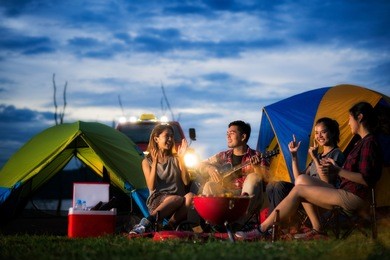 camping of asian man and women group, relaxing, sing a song and cooking, with ligh from car and tent
