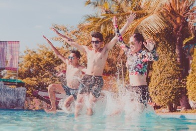 young people looking happy while jumping into the swimming pool together