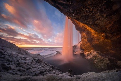 colorful sunset in cave behind seljalandsfoss waterfall in winter, iceland