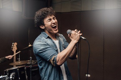 male lead vocalist singing in studio with music instrument background.
