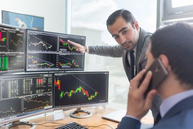 businessmen trading stocks online. stock brokers looking at graphs, indexes and numbers on multiple computer screens. colleagues in discussion in traders office. business success concept.