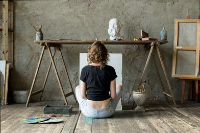 woman painter sitting on the floor in front of an empty canvas and drawing. art studio interior. horizontal drawing background. creative concept