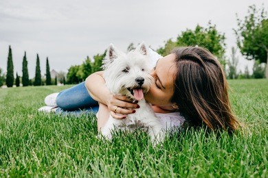 beautiful young woman playing with her little west highland white terrier in a park outdoors. lifestyle portrait.