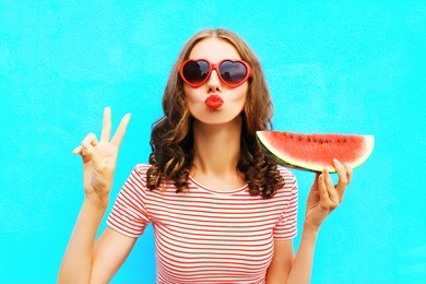fashion portrait woman is holding a slice of watermelon and blowing lips over a colorful blue background
