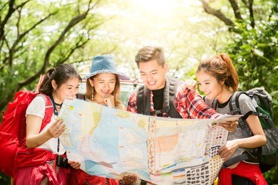 hiking - hikers looking at map. couple or friends navigating together smiling happy during camping travel hike outdoors in forest. young mixed race asian woman and man.