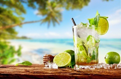 fresh mojito drink placed on wooden planks, blur tropical beach on background. summer drinks and beach vacation background