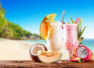 fresh fruit drinks placed on wooden planks, blur tropical beach on background. summer drinks and beach vacation background