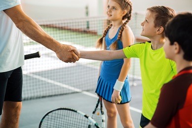 proud tennis coach praising kid by handshake